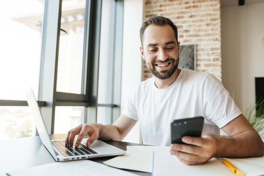 Image of man working with laptop and cellphone while sitting at table