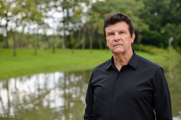 Portrait of mature handsome businessman relaxing at the park