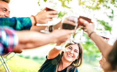 Obraz premium Hands toast with red wine - People having fun cheering at pic nic winetasting - Young friends enjoying harvest time together at farmhouse vineyard countryside - Focus on woman with blurred glasses