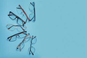 Set of corrective medical eyeglasses of various shapes lying on blue background with copy space