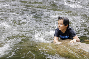 An elementary school boy was perched on a rocky stream at Kiriwong village. Khiri Wong village is a famous village of natural tourism in Thailand.