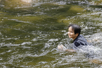 Obraz premium An elementary school boy was having fun playing in the fast flowing stream at Kiriwong village. Khiri Wong village is a famous village of natural tourism in Thailand.