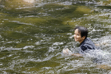 An elementary school boy was having fun playing in the fast flowing stream at Kiriwong village. Khiri Wong village is a famous village of natural tourism in Thailand.