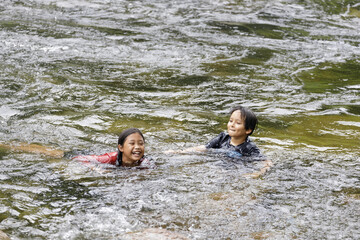A pair of elementary school boys and girls play in the rushing stream at Kiriwong village. Khiri Wong village is a famous village of natural tourism in Thailand.