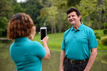 Happy mature multi ethnic married couple taking picture with phone together at the park