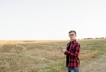 
young farmer stands on a cut field with a tablet in hand, agriculture management concept