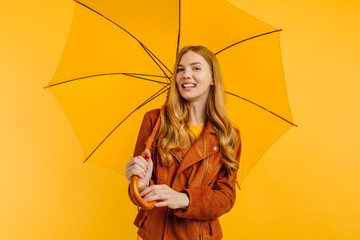 an attractive girl, in a bright yellow dress and an autumn jacket, stands with a yellow umbrella on a yellow background. Autumn concept