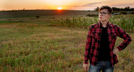 
A farmer in a shirt stands in a field at sunset