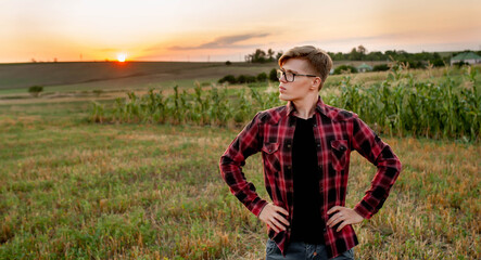 
A farmer in a shirt stands in a field at sunset