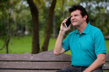 Portrait of mature handsome man talking on the phone at the park