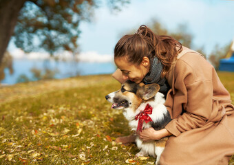 Autumn woman in coat tenderly embracing Welsh Corgi dog in autumn park, cute moments with pet. autumn wakks concept, friendship dog and human