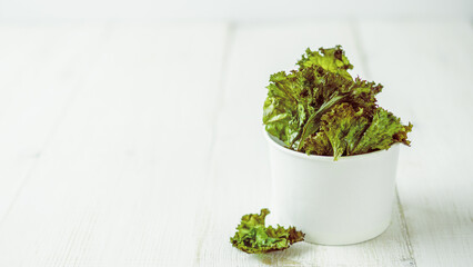 Kale Chips with salt in white paper cup. Homemade healthy snack for low carb, keto, low calorie...
