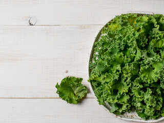 Kale close up. Green vegetable leaves, top view on white craft plate over white wooden tabletop....