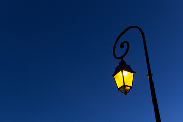 Fototapeta na wymiar yellow light of night street city spiral metal shape lamppost on blue sky background 