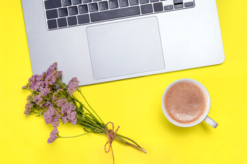 Holiday office desk composition - laptop, cup, bouquet of flowers on yellow table. Good morning concept