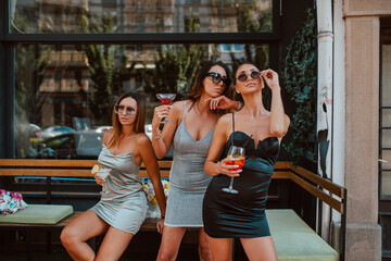 Three attractive caucasian women in short tight dresses are drinking cocktails in a cafe garden. Girls and party