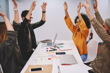 Diverse team of successful students holding hands up celebrating victory of startup project after brainstorming.Group of hipster guys happy with completed educational courses at meeting table