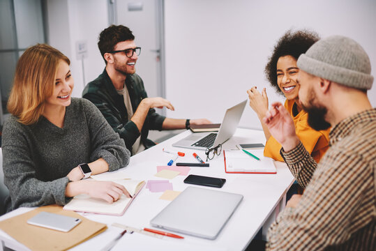 Positive male and female designers discussing creative ideas for developing startup project teamworking in office.Diversity group of cheerful hipsters students laughing during collaboration at desktop