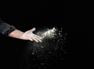 baker's male hand throws up a handful of white wheat flour on a black background