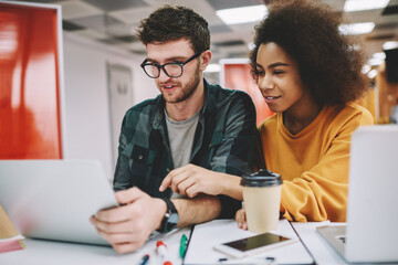 Multicultural male and female colleagues dressed in casual wear watching studying webinar on modern laptop computer using wireless internet connection.Diverse students searching information on website