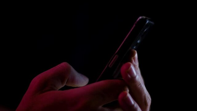 Thumb scrolling and typing on a smartphone close up in a dark room with red and white lighting
