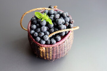 Blueberries with green leaves in a wicker basket on a gray background. Blueberry antioxidant. Healthy food and nutrition concept