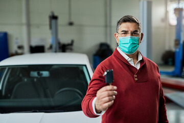 Fototapeta na wymiar Mid adult man with protective face mask holding car key in auto repair shop.