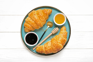 Fresh french croissants with chocolate on blue plate, blueberry jam, spoon, honey on white background Continental morning breakfast Top view Flat lay