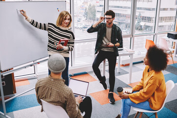 Young woman coach pointing on flip chart and explaining studying material group of multicultural students.Professional female teacher conducting workshop team of skilled young people in casual wear