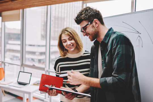 Young skilled woman consulting with qualified male coach during workshop in college.Positive colleagues dressed in casual wear collaborating with each other on studying task in modern office