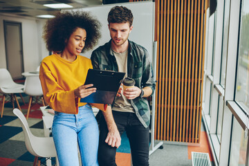 African american creative designer showing report caucasian colleague dressed in casual wear during working process in office.Collaboration of multicultural students on development of startup project