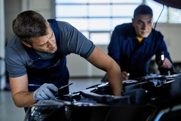 Auto mechanic repairing car engine with a coworker in a workshop.