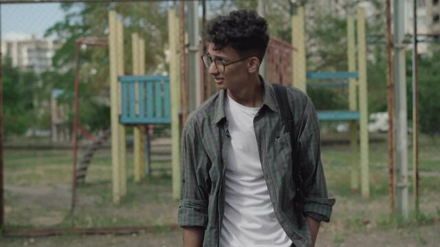 Front view of two Caucasian hooligans laughing at shy mixed-race guy walking behind and leaving. Portrait of embarrassed young bullied man walking outdoors in 1980s. Retro lifestyle.
