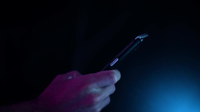 Thumb scrolling on a smartphone in a dark room with purple and blue lighting