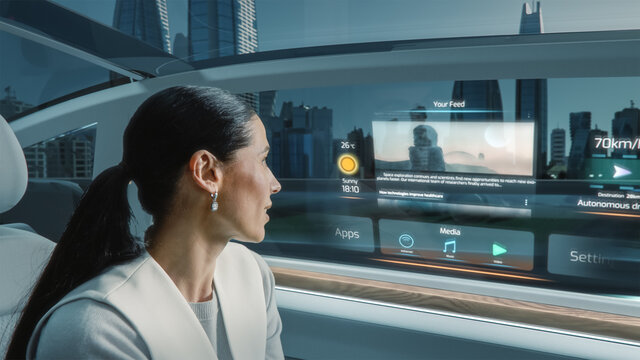 Shot of Attractive Female Reading the News on a Futuristic Augmented Reality Interface while Riding in an Autonomous Self-Driving Car. Modern City with Glass Skyscrapers in a Car Window. - Powered by Adobe