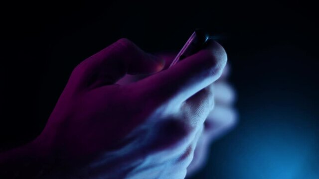 Thumb scrolling on a smartphone in landscape close up in a dark room side profile with purple and blue lighting