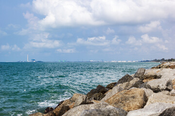 A view of the green sea, blue sky, cloudy sky, and rocks at the right corner of the picture.