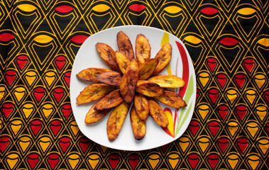 A plate of fried plantain or dodo creatively served on a colorful african pattern table cloth © Afrofresh