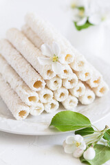 Obraz na płótnie Canvas Delicate sweet cookies in the form of tubes in coconut flakes filled with vanilla cream on a white plate. 