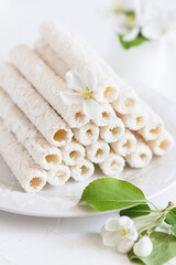 Delicate sweet cookies in the form of tubes in coconut flakes filled with vanilla cream on a white plate. 