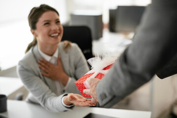 Young businessman giving his colleague present in office. Young man suprise beautiful businesswoman in office.