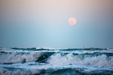 wild sea with full moon in background, focus on big wave