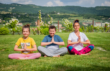 Mother and her children doing yoga exercises outdoors - Young woman doing fitness exercises in the park - Achieving harmony
