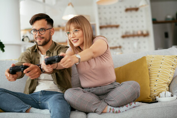 Husband and wife playing video game with joysticks in living room. Loving couple are playing video games at home..