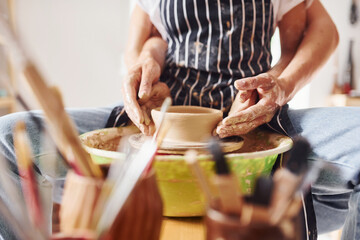 With her boyfriend or husband. Close up view of young female ceramist that indoors with handmade clay product. Conception of pottery