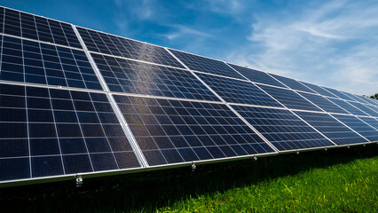 Solar power plant panels on a green meadow against a blue sky with clouds