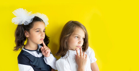 Two serious and dreamy schoolgirls. cute caucasian girls with brown and blond hair on yellow background. The concept back to school. Copy space