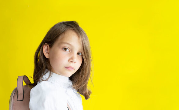 serious pretty schoolgirl. cute caucasian girl with blond hair with backpack on her back on yellow background. The concept back to school. Copy space