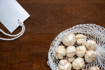 Garlic in a net bag and white paper tag placed on a wooden background