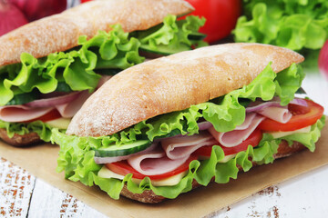 Two sandwiches with fresh vegetables, ham and cheese in ciabatta bread	